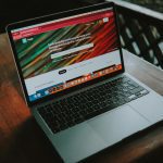 A close-up view of a laptop with a website open, placed on a wooden table near a window.